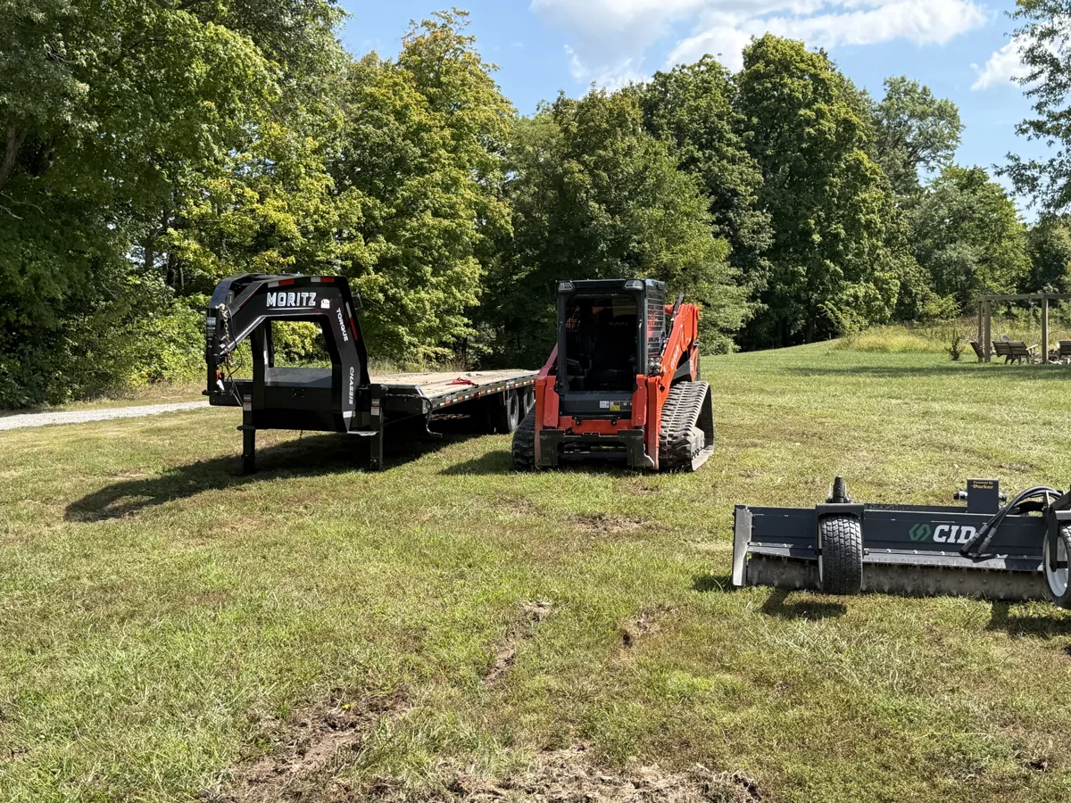 Ground Force Land Solutions compact track loader with a brush cutter attachment beside its equipment trailer on a job site