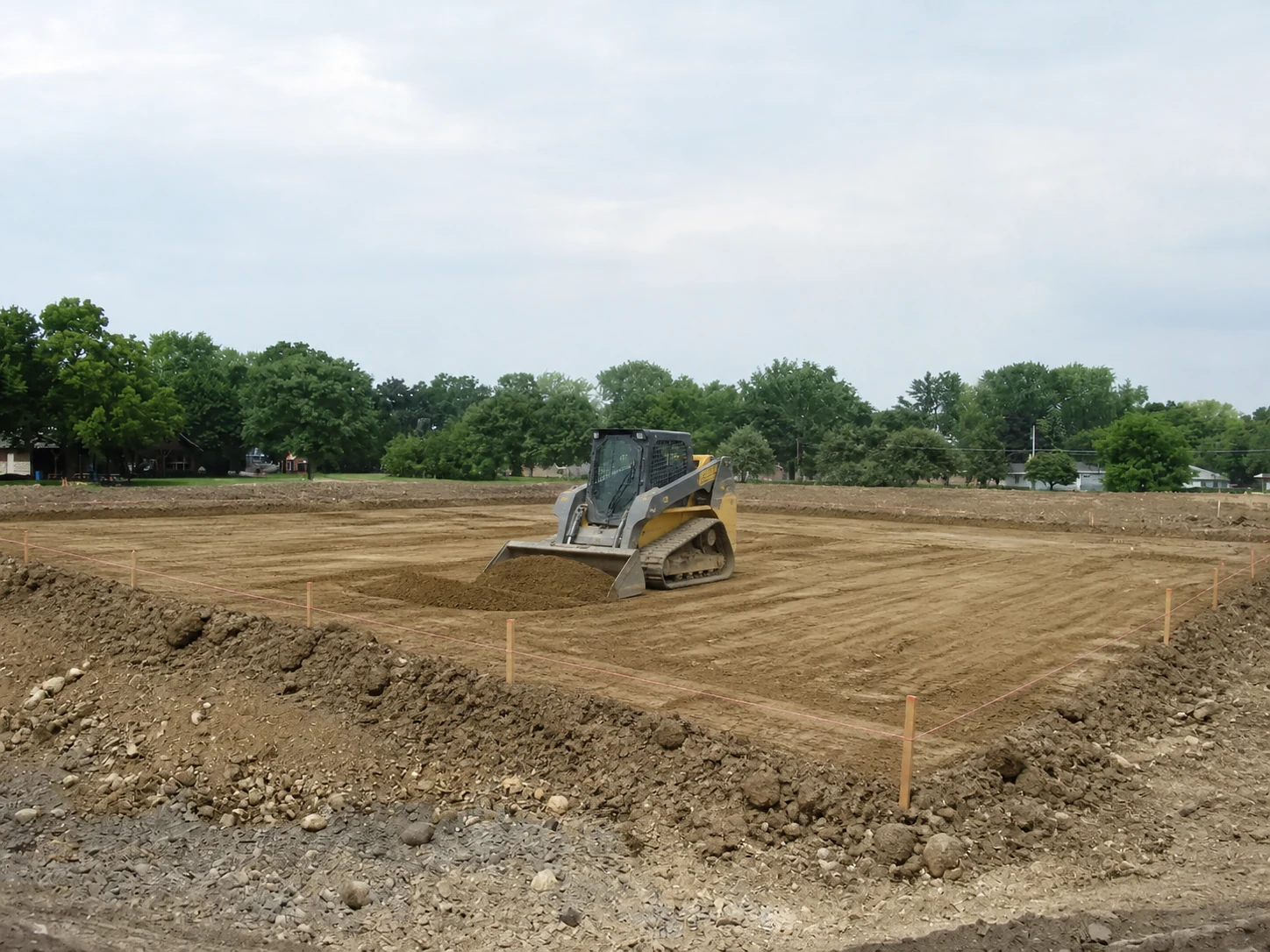 Tracked skid steer grading a staked dirt pad for a future house foundation